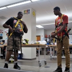 Two high school students demonstrate how to correctly wear a safety harness during a class presentation.