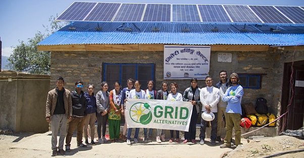Nepali women hold a GRID banner in front of their birthing center, where solar panels are visible on the roof