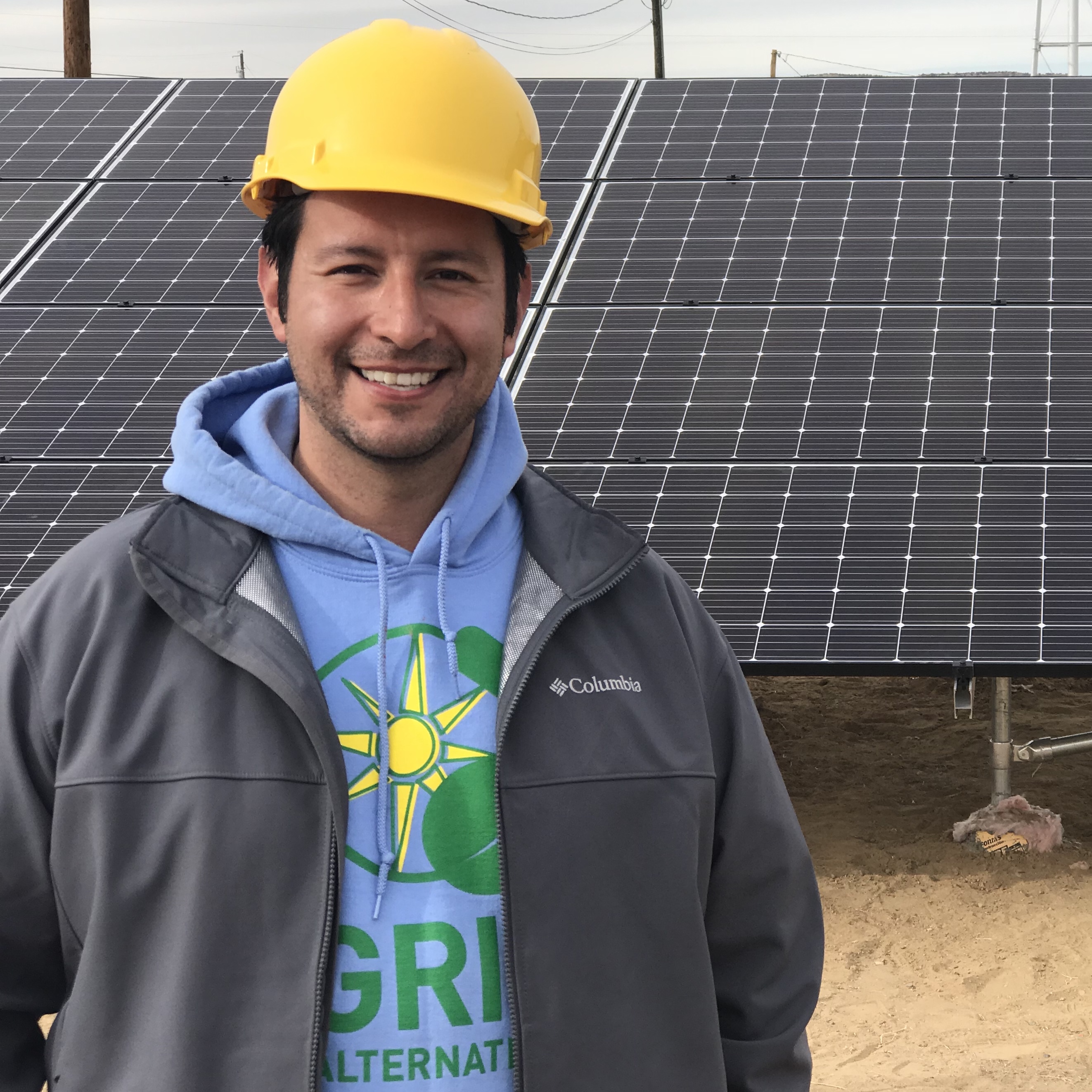 Adam Bad Wound, in GRID shirt and hard hat, in front of a ground mount system