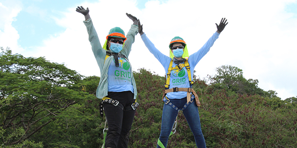 Two GRID installers, masked and harnessed for safety, throw their arms in the air