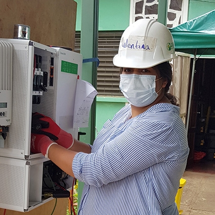 Valentina, in mask and hard hat, works at an electrical panel