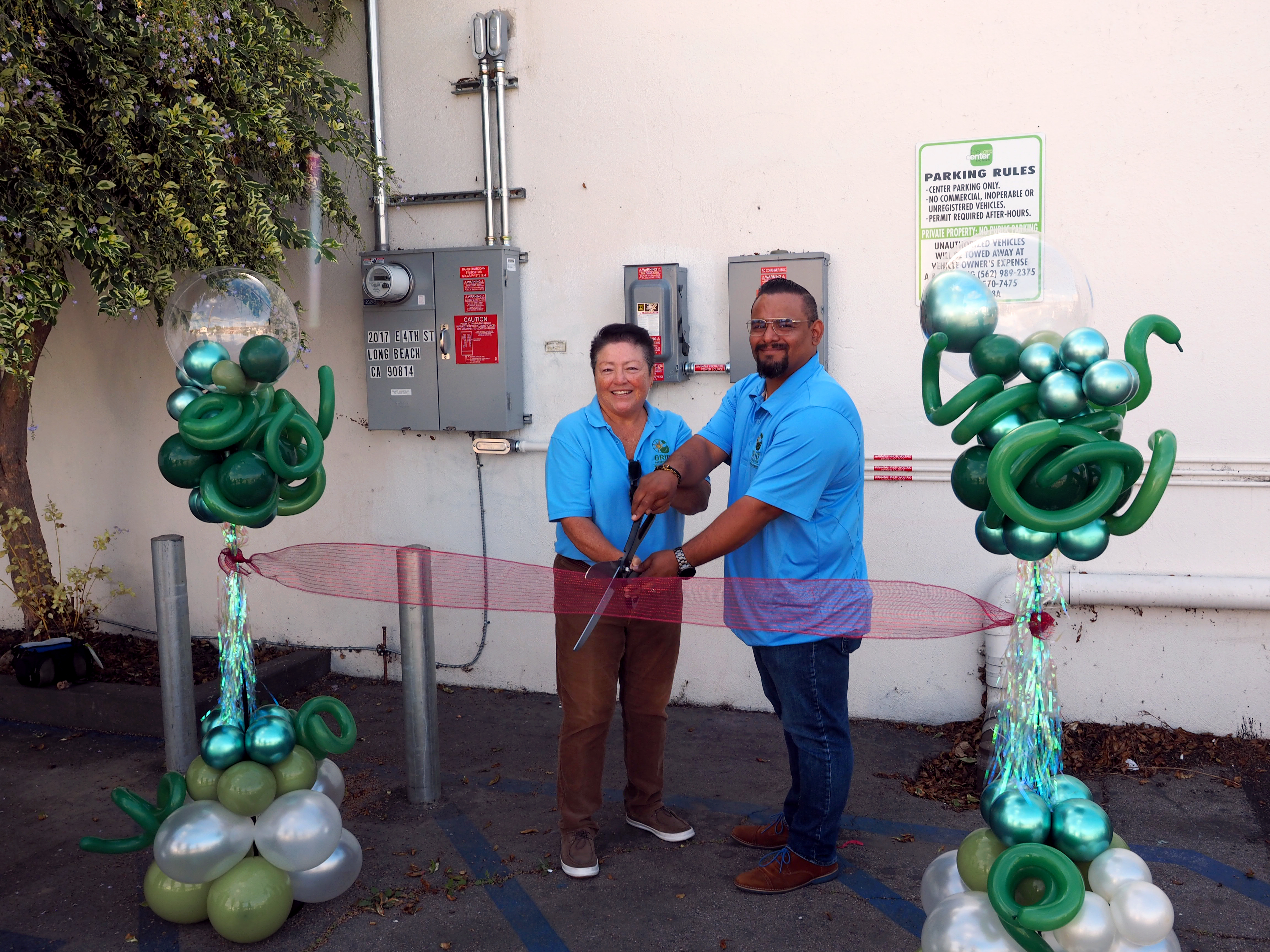 GRID GLA Staff Cutting a Ribbon in front of a new Electric Panel that Powers the LGBTQ Centers Solar System