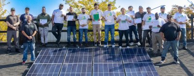 group of men posing for photo on a mock roof with solar panels