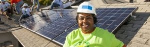 Smiling client in front of her solar panels, while installation continues in the background