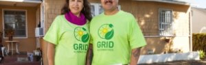Clients in green GRID t-shirts smile in front of their solarized home