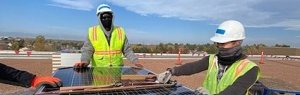A picture of three people standing around a stack on uninstalled solar modules with their PPE gear on.. 