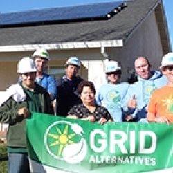 Homeowners and GRID staff and trainees holding a GRID banner in front of the home where solar panels are visible in the background