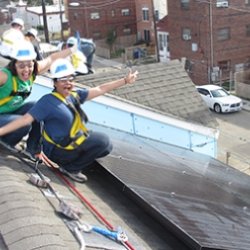 GRID solar installers on rooftop with solar panel, arms in the air