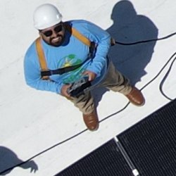 Jose Montes looking up and smiling on a rof next to a solar panel