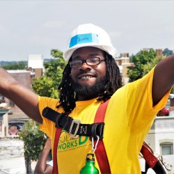 Devonte, a Solar Works DC trainee, puts his arms in the air while on the roof during a solar installation.