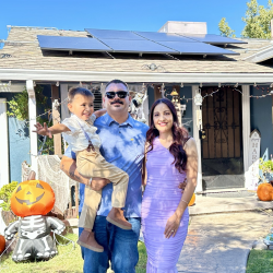 GRID NV client Christian Romo and his wife and son in front of their home with solar panels visible behind them.