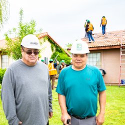 Two men wearing hard hats posing for photo in front of a home