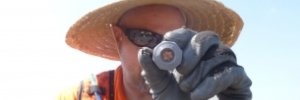 Volunteer in a large straw hat and sunglasses holds up a piece of conduit to the camera