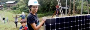 Nicaraguan community participants cross a field with solar panels and other equipment