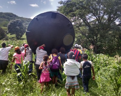 Participants and members of the Cruz family in Nicaragua move a water barrel through a field