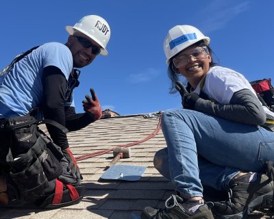 Volunteer and GRID staffer on the roof smiling and throwing peace signs: it takes two