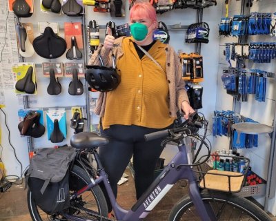 An Electric Bike program beneficiary stands next to her new E-bike at the Watershed Workshop, a community based organization that has partnered up with GRID Alternatives Bay Area's Clean Mobility Program