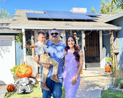 GRID NV client Christian Romo and his wife and son in front of their home with solar panels visible behind them.