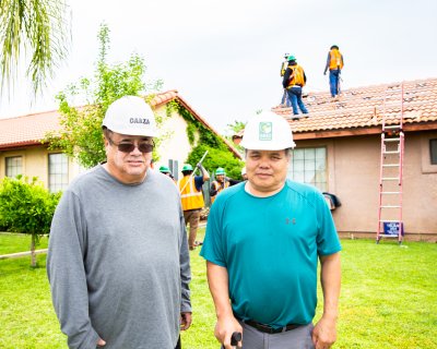 Two men wearing hard hats posing for photo in front of a home
