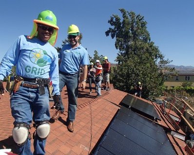 GRID staff in hard hats smile next to a newly installed rooftop solar array.