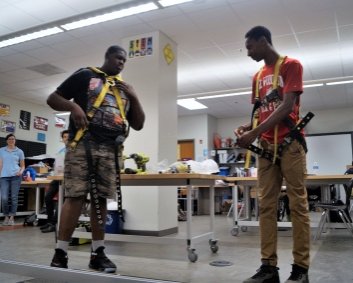 Two high school students demonstrate how to correctly wear a safety harness during a class presentation.