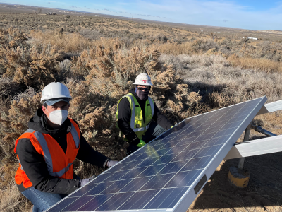 Daniel Ponton on a solar install. Two men in safety gear with grassy plains in the background.