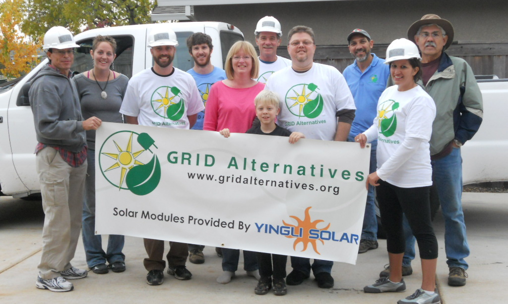 Group of GRID Alternatives and Ying Solar workers holding banner at solar installation site with white van in background