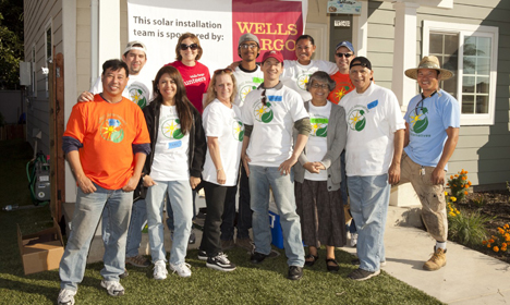 Group of volunteers in solar installation t-shirts standing in front of a house with Wells Fargo banner visible