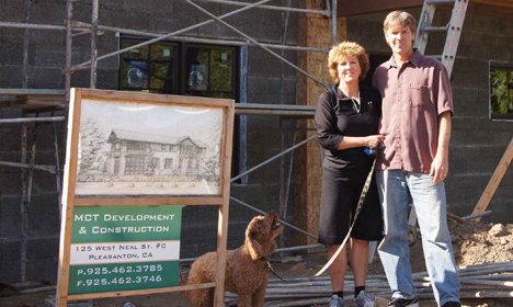Jon and Kitty Harvey stand with their dog beside an architectural sketch and MDT Development sign at a construction site
