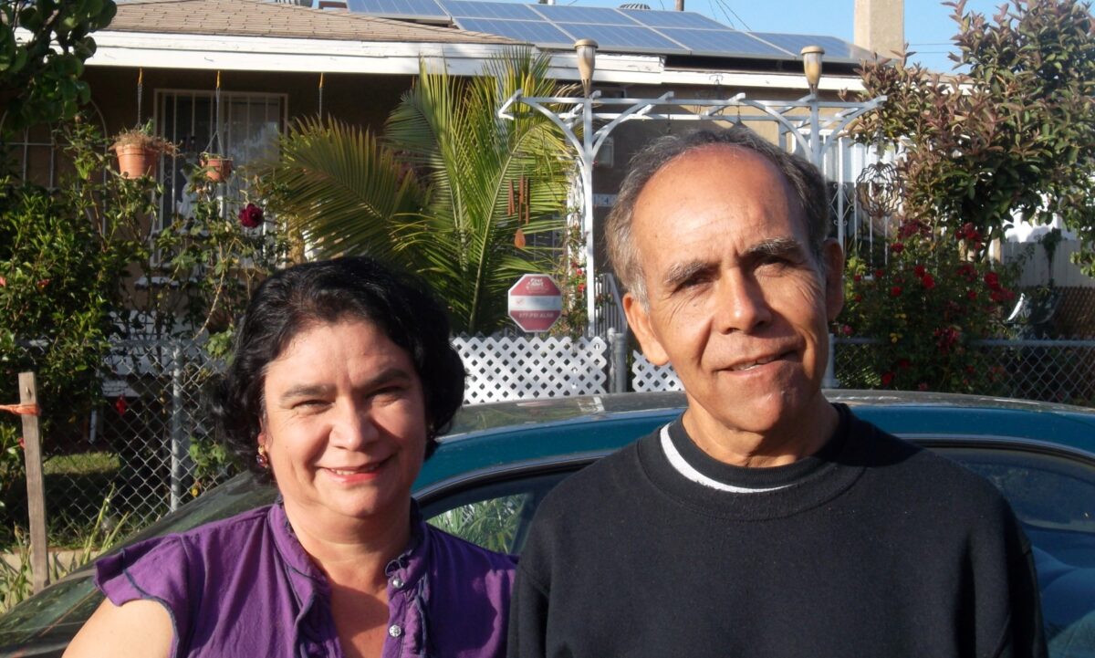 Two people smiling in a residential backyard with solar panels and pool visible behind them
