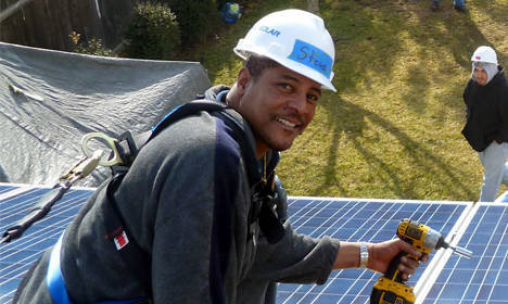 Worker in safety helmet installing solar panel on roof with tools