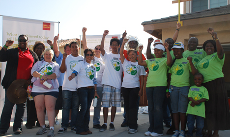 Group of diverse children and adults wearing green and white shirts with raised fists celebrating outdoors at a solar energy community event