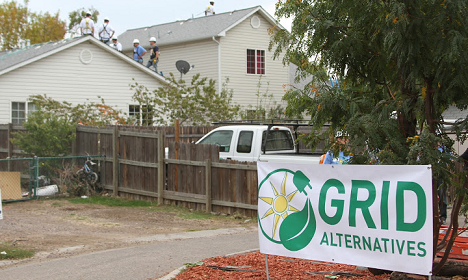 GRID Alternatives sign in front of residential house with workers on roof