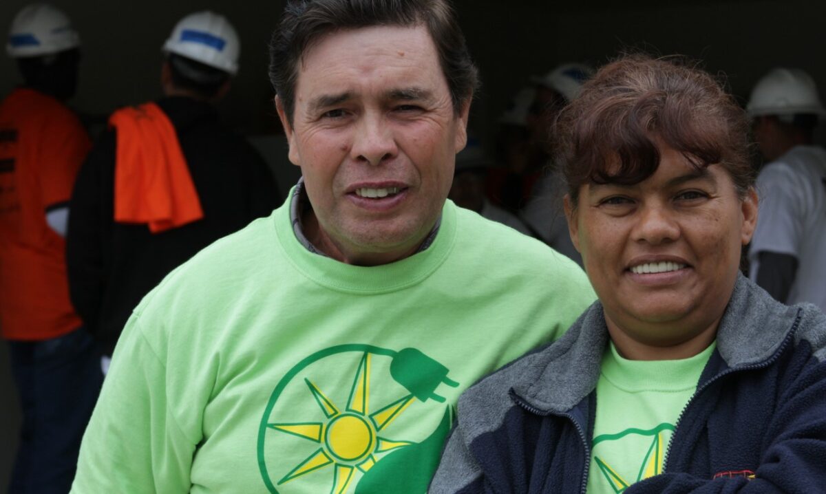 Two people wearing matching green shirts with sun and leaf logo at outdoor community event