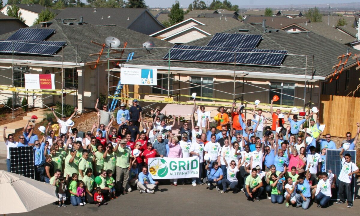 Large group holding GRID Alternatives banner in front of solar panel-equipped house during community event