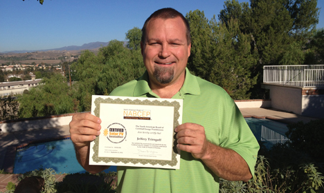 Man in green shirt holding certificate by pool with landscape view behind him