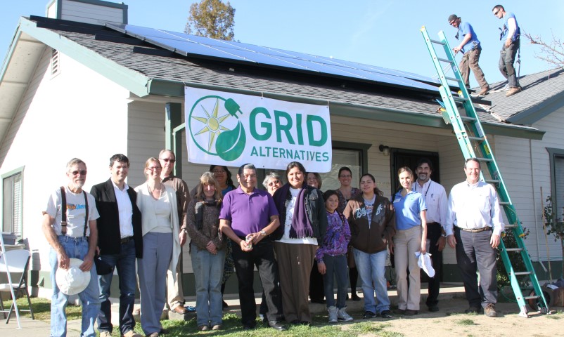 Group posing in front of house with Grid Alternatives solar panel banner and EPA Climate Change Champion award