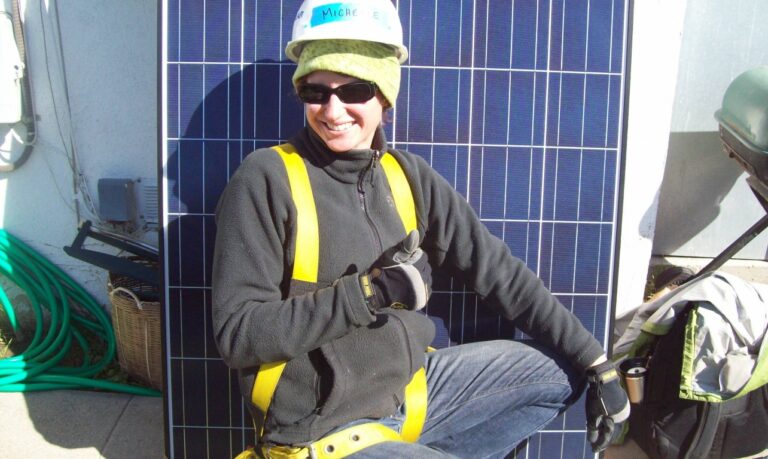 Woman in safety gear crouching in front of solar panels during installation