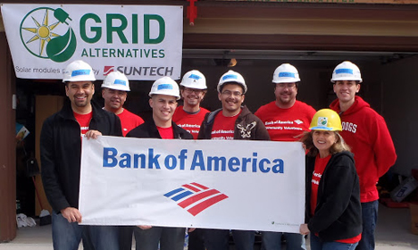 Bank of America volunteers in hard hats holding company banner in front of Grid Alternatives solar installation site