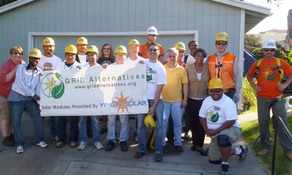 Group of workers in hard hats holding GRID Alternatives banner with solar modules provided by Yingli Solar