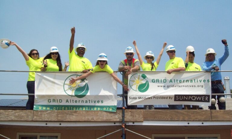Team of workers in safety gear holding GRID Alternatives and Sunpower banners on a rooftop