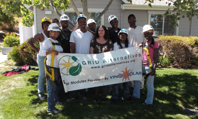 Group of workers in hard hats holding GRID Alternatives banner at residential solar installation site in Marin