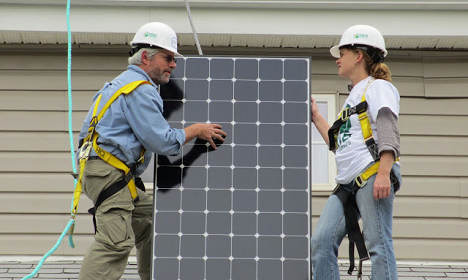 Two workers in safety gear installing a solar panel on a residential roof