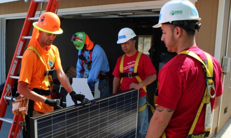 Four workers in safety gear discussing a solar panel installation outdoors