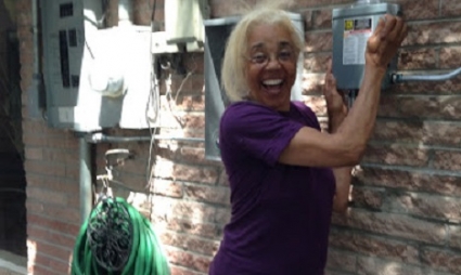 Woman in purple shirt smiling while standing next to green coiled hose on brick wall