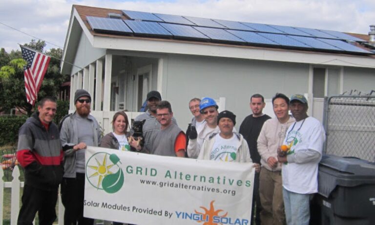 Group of volunteers with Grid Alternatives banner in front of house with solar panels installed on roof
