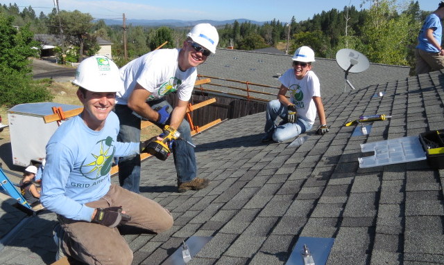 Four volunteers in white hard hats installing solar panels on a residential roof during a community service project