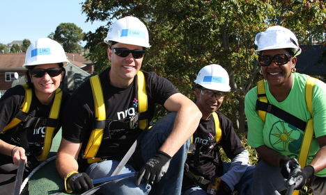 Five construction workers in hard hats and safety vests stand together smiling at a work site
