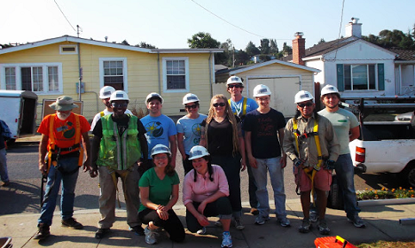 Group of construction workers in hard hats and safety gear standing together in front of houses