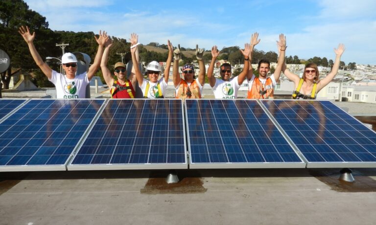 Team of professionals celebrating on rooftop with solar panels installed behind them